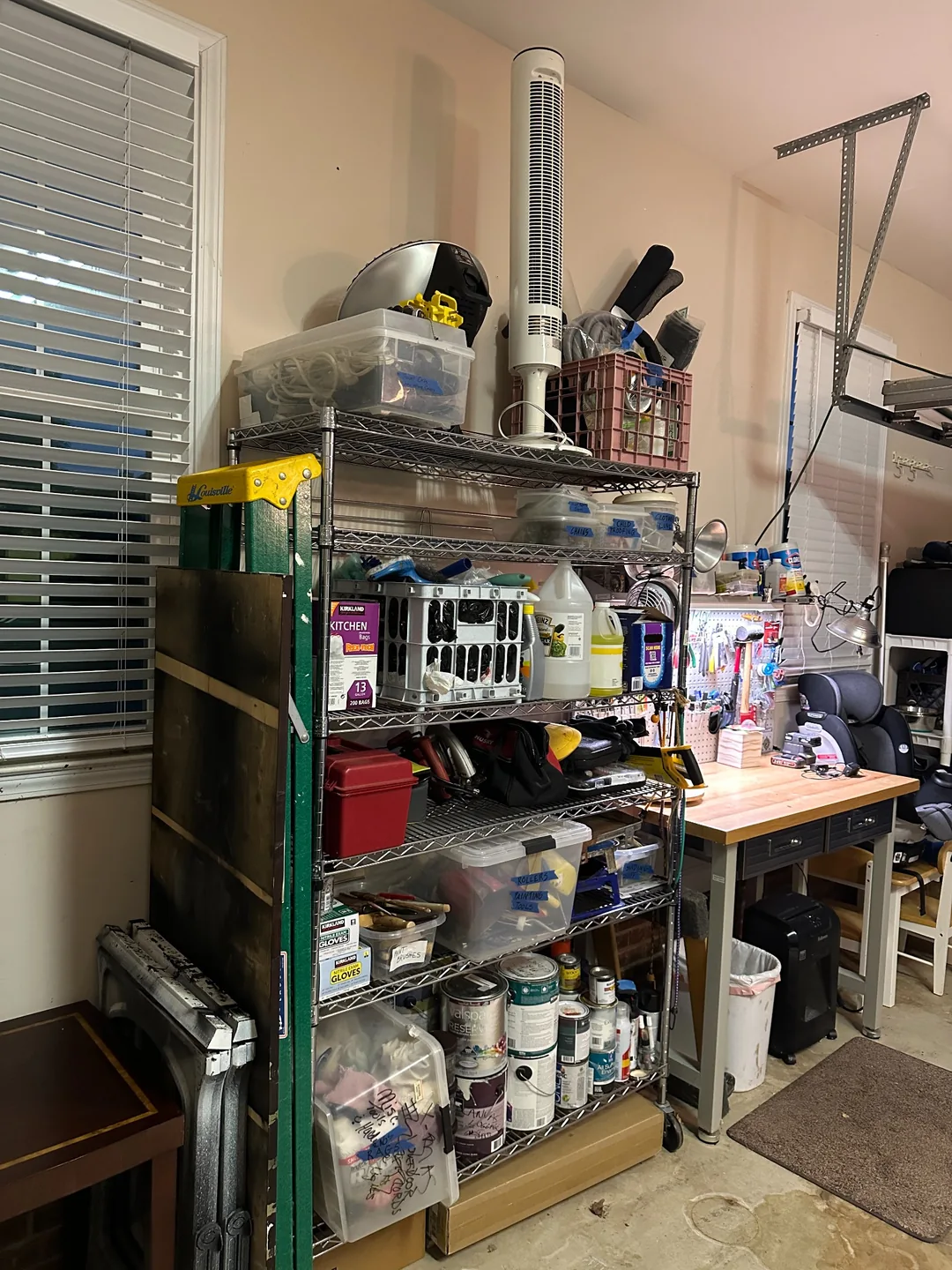 Labeled tools and supplies grouped on garage shelving beside a workbench.