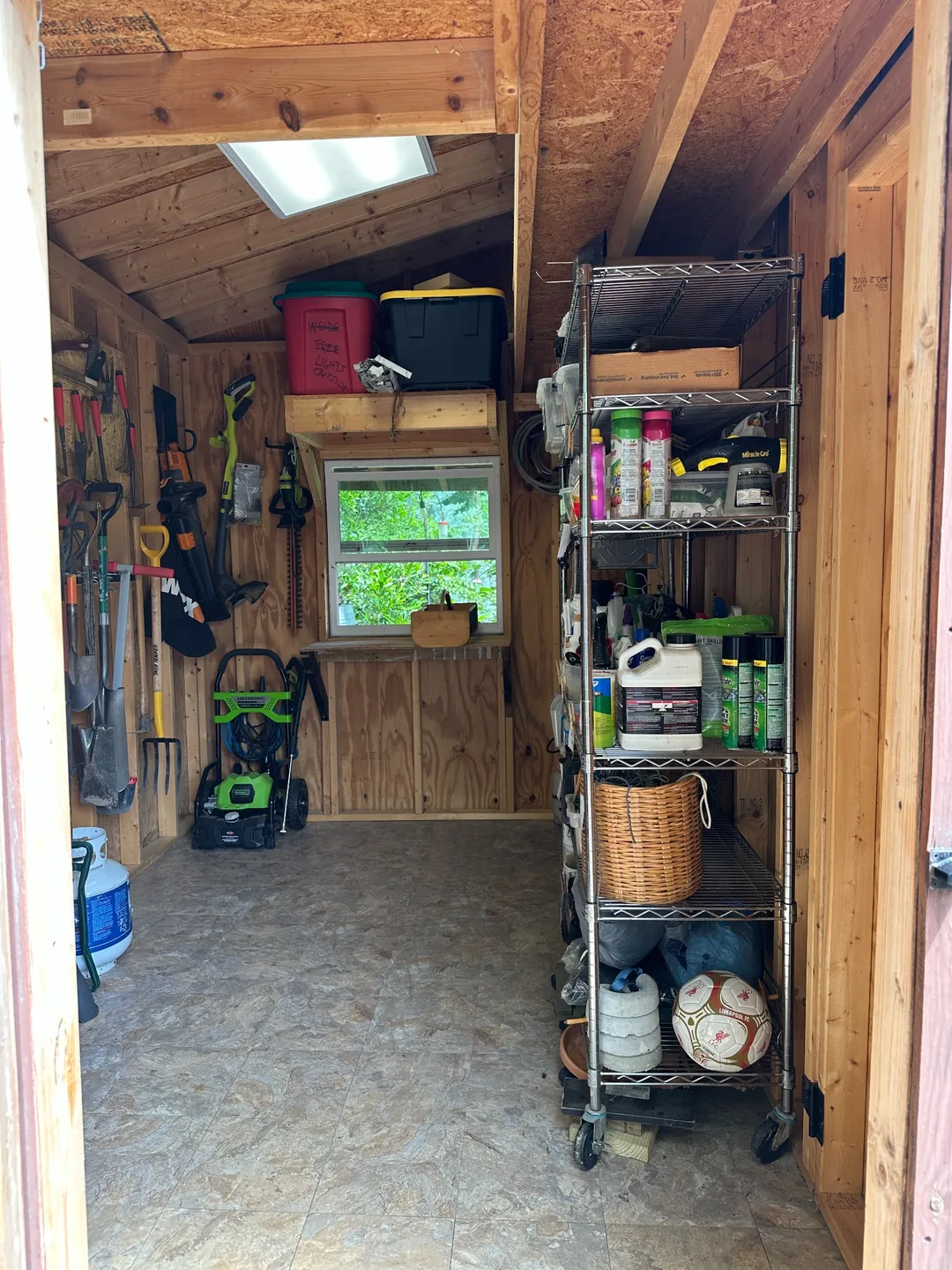 An organized garden shed with tools along the wall and an open central aisle.